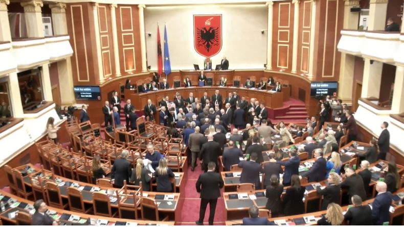 10:50 Karrige të kthyera përmbys, bllokim foltoreje dhe goditje e tavolinave nga deputetët e PD, çfarë po ndodh në Kuvend, Peleshi lexon me shpejtësi nenet